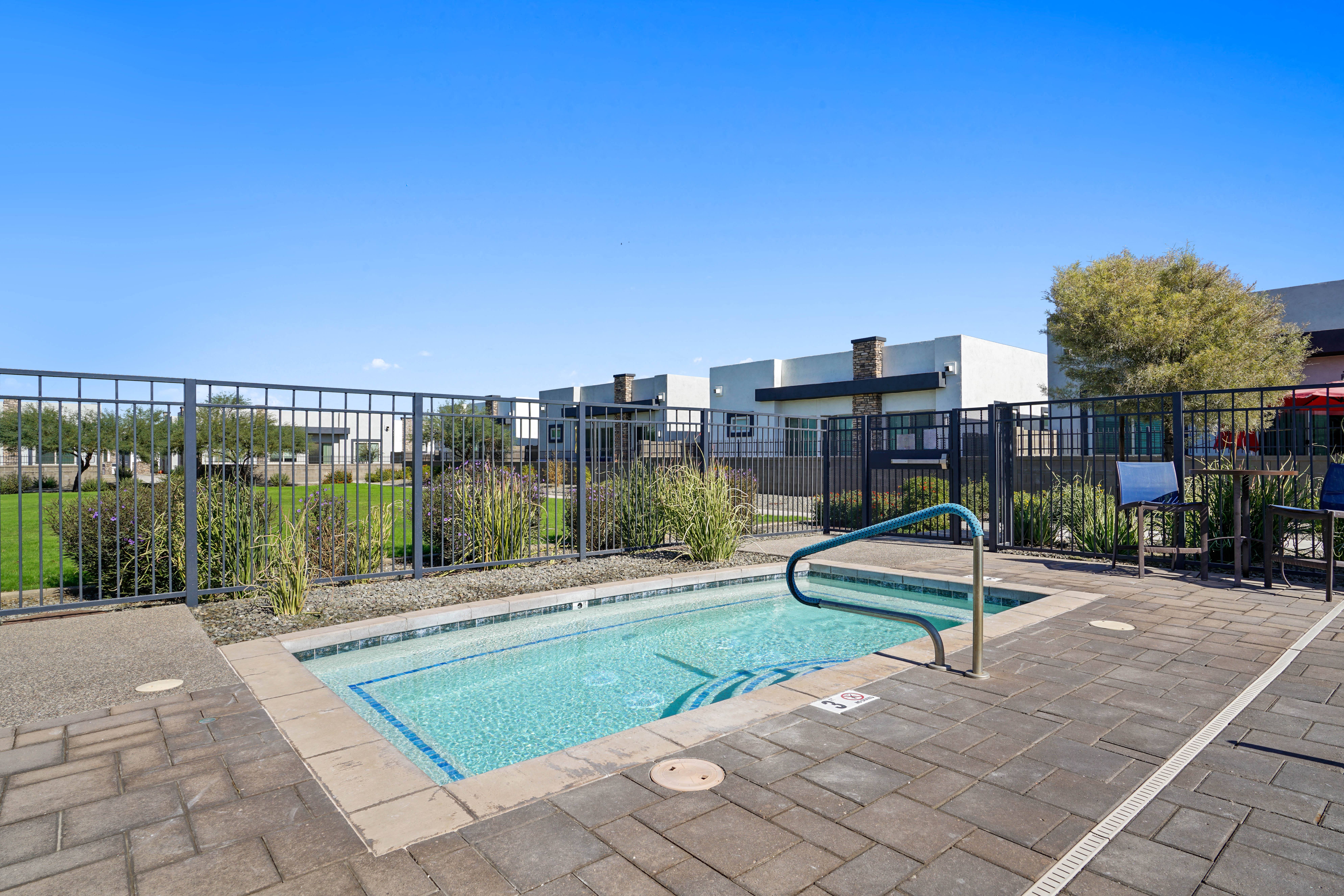 a swimming pool with a metal fence around it and a building in the background at Olive Queen Creek Apartments, Arizona